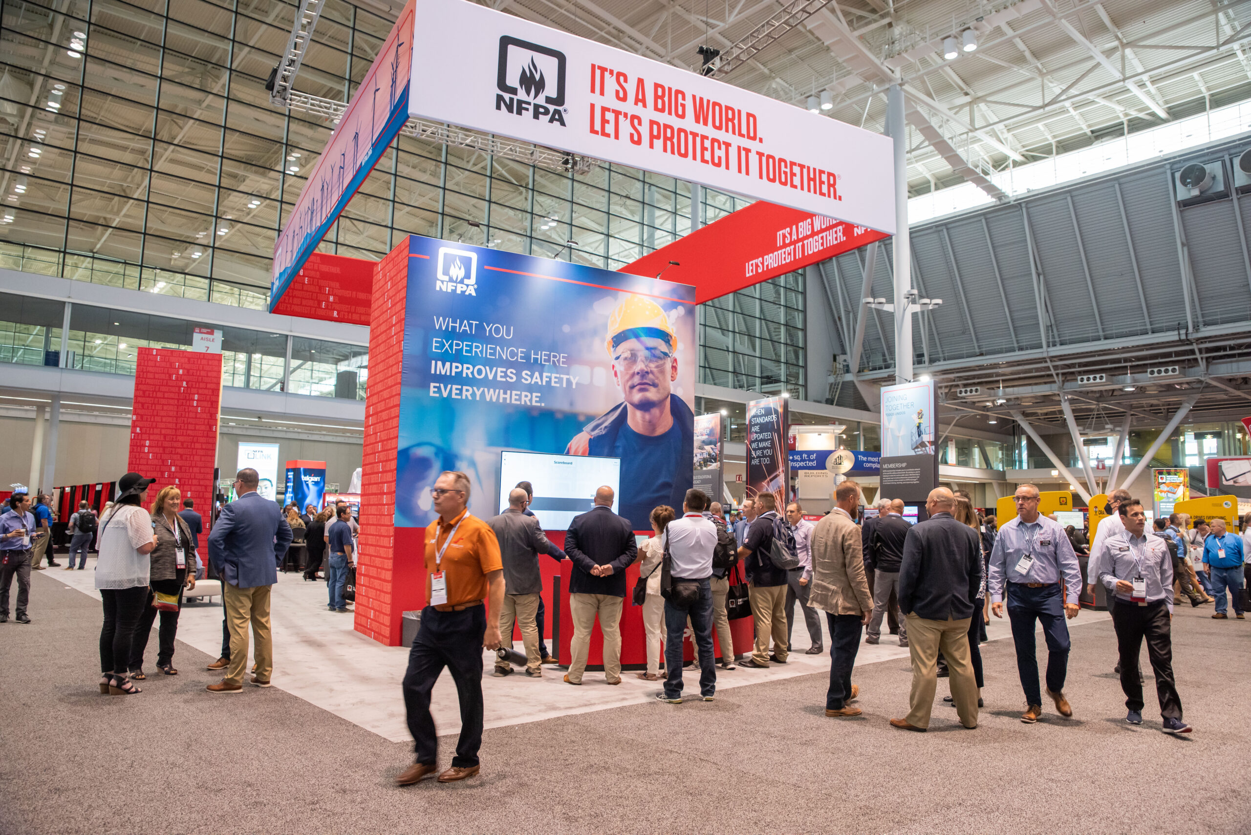 Busy trade show hall with NFPA booth, red and blue displays, and attendees walking around.