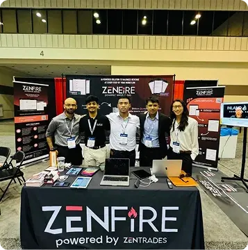 Five people stand behind a conference booth for ZenFire, with laptops and marketing materials on the table, and ZenFire banners in the background.