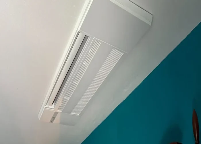 White rectangular ceiling vent with slatted diffuser along a white ceiling in a teal-walled room.